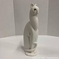 Full view of the tall white pebbled cat figurine with a winking expression, standing upright.