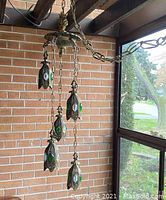 Side view of lamp showing five hanging leaf-shaped shades with green and clear glass inserts and brass-tone chains.
