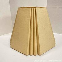 Front view of the beige geometric polygon shaped fabric lamp shade showing its structured five-sided panels and pleated fabric design.