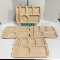 Top view of four beige vintage school cafeteria trays showing multiple compartment design.