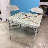 Vintage Punkinhead childs folding card table with 2 folding chairs shown from perspective view in room.