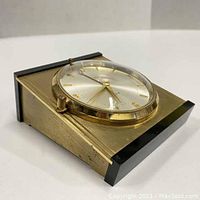 Side angle showing the windup desk alarm clock with gold-tone metal body and black trim.