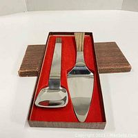Original box with red felt lining containing two serving utensils with teak handles and stainless steel heads, shown from top view.