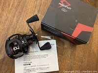 PISCFUN Torrent 247 Baitcasting Reel with original box, manual, and small wrench on wood surface.