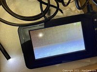 Close-up photo of the digital inspection endoscope display screen showing a live feed, connected to a flexible inspection camera cable with LED lights at the probe tip.