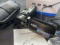 Photo showing the black HD video camera with its lens extended, user manual, and case visible in the background