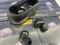 Two black Zeus Air earbuds placed on four unopened retail boxes of Zeus Air True Wireless Stereo Earbuds, showing packaging and branding.