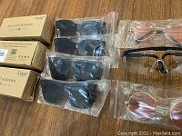 Top view of all glasses laid out, includes box packaging for blue light blocking glasses, 3 large black sunglasses, 2 round rose-tinted sunglasses, and a pair of clear protective glasses.