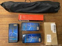 Full-size tripod in black bag with five boxed tripod-related items on wood floor.