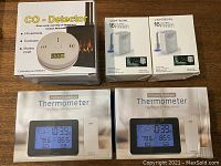 Lot showing all 5 items: CO detector box, 2 indoor/outdoor thermometer boxes/manuals, and 2 Lightbowl nightlight boxes.