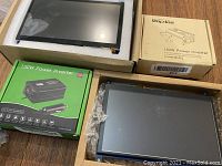 Raspberry Pi screens in protective packaging alongside two power inverter boxes on wooden surface.