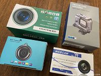 Four boxed webcams and accessories including GoPro housing and multiple USB webcams
