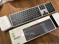 Rii multimedia wireless keyboard in silver and black with numeric keypad alongside the wireless mouse in its box on a wooden table.
