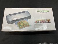 Closed box showing Geryon vacuum sealer with a sealed bag of vegetables, branding and features.