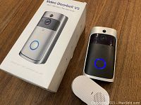 Video Doorbell V5 device shown with its box and wireless chime accessory on a wood surface.