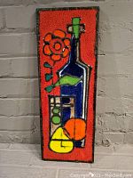 Front view of rectangular hand-made decorative tile with abstract design in bright colors including blue bottle, red flower, and fruits, on orange background, glazed surface.