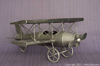 Side angle of the tin metal bi-plane model showing detailed fuselage, wings, wire struts, propeller, and wheels.