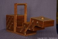 Angled view showing fold-out compartments of the wooden sewing box extending outward, highlighting the segmented sections and the carrying handle.