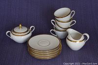 Porcelain tea set components arranged on dark purple fabric including stacked cups and saucers, creamer, and sugar bowl with gold pattern detailing.