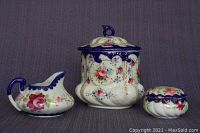 Front view of the biscuit jar, sugar bowl, and creamer showing floral decorations and cobalt blue rim