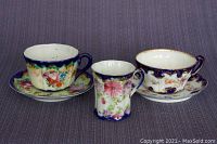 Three antique Nippon porcelain cups displayed with two matching saucers, showing floral patterns and gold accents