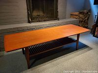 Full view of rectangular teak coffee table on carpeted floor in front of brick fireplace