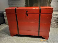 Closed view of the front red painted pine blanket chest with black metal straps and lock.