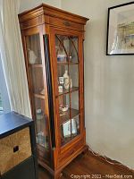 Full-height view of wooden curio cabinet with glass door and shelves