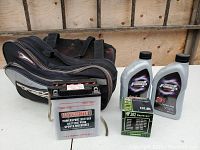 Items include Motomaster Powersport motorcycle battery with mounting bracket, Technik saddlebag, two bottles of Motomaster Formula motor oil, and a boxed oil filter.