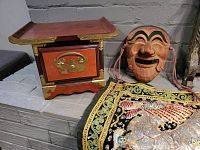 Photo showing mini Korean single drawer chest, carved wood Korean mask, and embroidered wall hanging