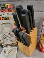 Knife block with nine black-handled knives, one slot empty, next to boxed multi grater and slicer.