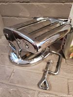 Side view of the stainless steel manual pasta maker with clamp attached for countertop use