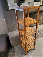 Full view of the tall, slim five-tier wooden shelving unit near a brick wall and fireplace.