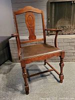 Front-left view of antique captain's chair showing wooden details and leather seat.
