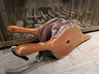 Photo showing side view of vintage fireplace bellows with wooden handle, leather sides, and metal rivets.