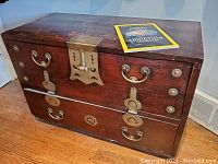 Front view of the vintage two-drawer chest showing reddish wood and metal handles, large metal latch in the center.