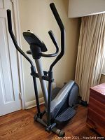 Side view of the elliptical trainer showing the full unit with handle grips and foot pedals.