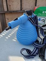 Blue Steam Genie handheld steam cleaner with black top and striped strap on white surface.