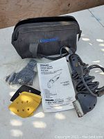 Top view showing contour sander, sanding pads, user manual, and carrying bag on a light surface under sunlight.