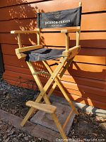 Side angle view of director's chair showing natural wooden frame, armrests, footrest and torn black canvas seat with Jackson Triggs printed backrest.
