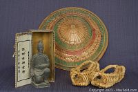 Chinese terracotta warrior figurine in a box, standing in front of a large decorated Thai straw hat with two pairs of Korean straw sandals in front.