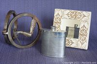 Cast iron door knocker, pewter flask, and decorative mirror on fabric background.