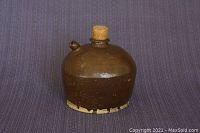 Front view of antique ceramic saki jug with cork stopper and short spout against blue fabric background.