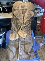 Front view of brown leather jacket with thick tan fur collar and cuffs, hanging on a hanger