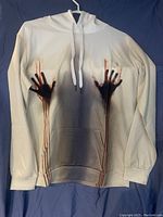 Front view of white hoodie showing black handprint and red dripping paint design with white drawstrings and front pouch pocket