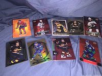 Lot of 8 hockey cards laid out on blue fabric with various designs and colors. Cards feature players in action poses wearing NHL team uniforms.