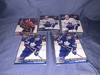 Five hockey cards with players Auston Matthews, William Nylander, and Matthew Tkachuk, arranged on a blue fabric background.