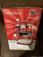 Photo of the unopened box of WestBend Theater Crazy 4 Qt Theater Style Popcorn Machine showing red retro theater style design and popcorn graphics.