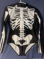 Front view of black long sleeve leotard with white skeleton ribcage and pelvic bone print hung on hanger.