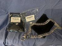 Photo of a silver-tone metal wallet chain with two black fabric pouches on a blue cloth background. Both pouches are new in packaging with barcode labels.